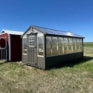 Exterior of a small greenhouse with polycarbonate sides and roof, with brown accents on the bottom of the walls.