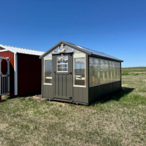 Exterior of small greenhouse with polycarbonate sides and brown trim around the base.